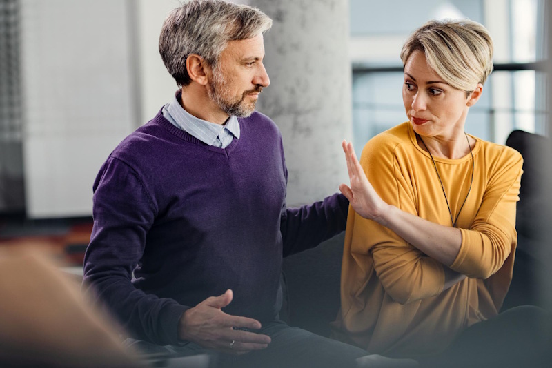 Erfolgreicher Mann Mitte 40 im Konflikt am Küchentisch, Partnerin wendet sich ab – Szene für eskalierenden Streit mit der Partnerin